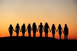 Sunrise silhouette of 10 young women walking hand in hand.